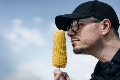 Mid adult man eating corn against cloudy sky