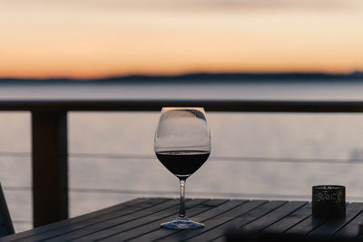 Close-up of wineglass on table against sea during sunset