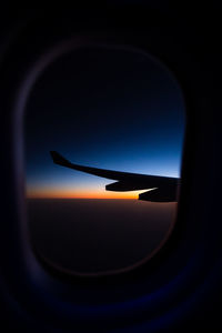 Silhouette airplane wing seen through window against sky during sunset