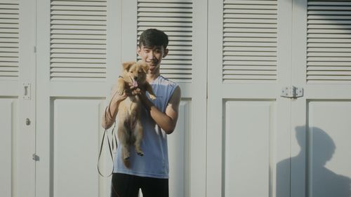 Portrait of man holding dog against closed door