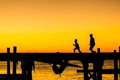 Silhouette men on pier against sky during sunset