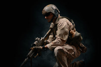 Man wearing helmet holding rifle against black background