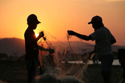 Silhouette fishermen working with net at beach during sunset