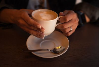 Hands holding white cup with coffee. cappuccino with latte art in female hands with french manicure 