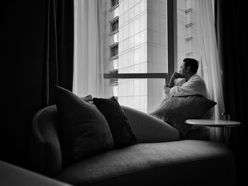 Thoughtful mid adult man looking through window while sitting at home