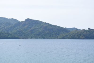 Scenic view of sea by mountain against clear sky