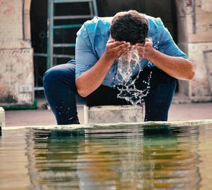 Man cleaning face at fountain in city