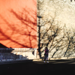 Woman walking on footpath by bare tree