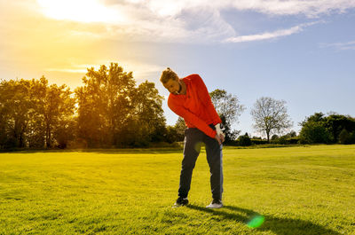 Man playing golf on course against sky during sunny day