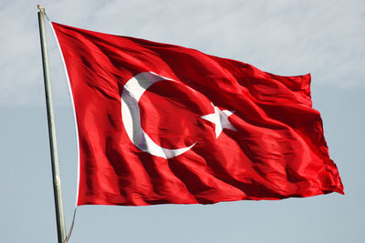 Low angle view of flag on red umbrella against sky