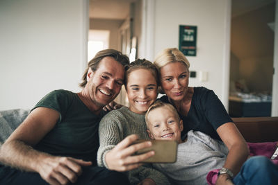 Smiling family taking selfie through smart phone while sitting on sofa at home