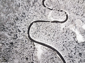 Curvy windy road in snow covered forest, top down aerial view.