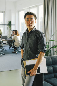 Portrait of confident businessman holding document while standing in office