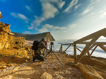 Man sitting on rock by sea against sky