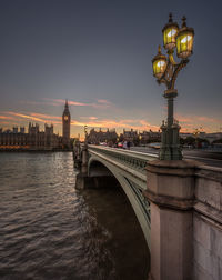 Westminster bridge over thames river by big ben and houses of parliament against sky during sunset