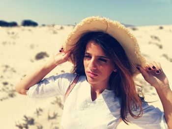 Beautiful young woman holding hat at beach on sunny day