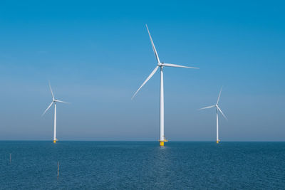 Windmills by sea against clear sky