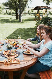 Family and friends having meal - pizza, salads, fruits and drinking white wine during summer picnic