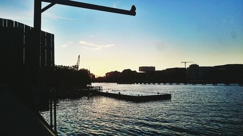 Silhouette buildings by river against sky during sunset