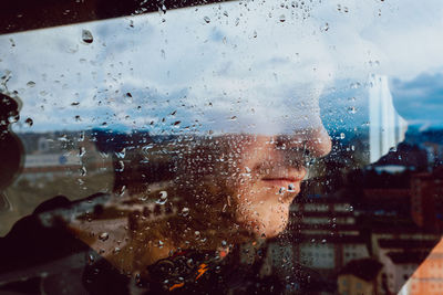 Portrait of man seen through wet glass window in rainy season