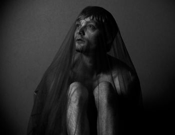 Shirtless man covered in netting while sitting against gray background