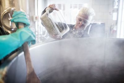 Female pouring ingredients in container while assisting coworker at factory