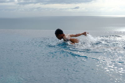 Teenage boy swimming in infinity pool against sea