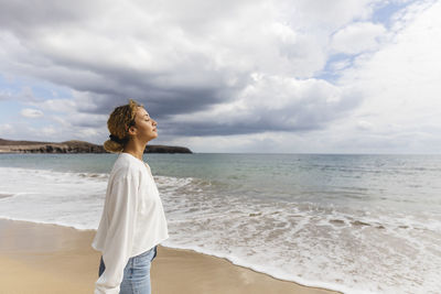 Woman with eyes closed standing by sea at beach