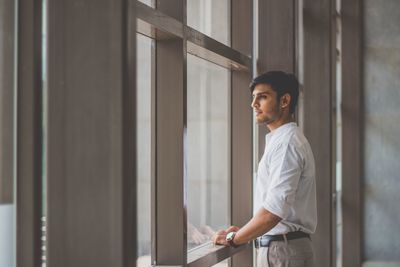 Side view of young man looking through window