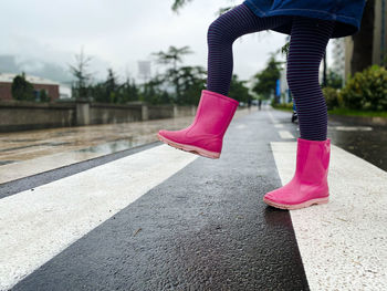 Child legs in pink rain boots on crosswalk