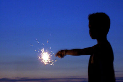 Silhouette of woman holding fireworks against sky at night