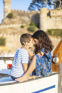 Side view of siblings embracing while sitting on railing