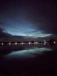 Illuminated lights by sea against sky at night