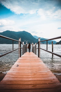 Rear view of woman standing on pier over lake against sky