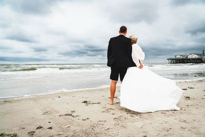 Rear view of couple walking on shore against sky