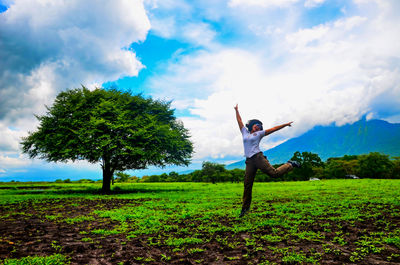 Man with arms outstretched standing on field against sky