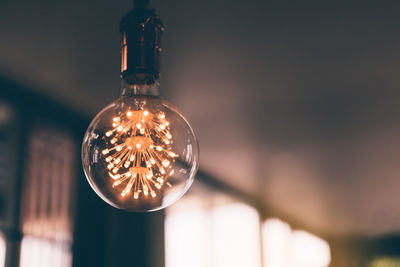 Close-up of illuminated light bulb hanging from ceiling