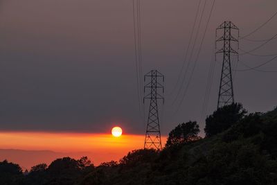Low angle view of silhouette electricity pylon against sky during sunset