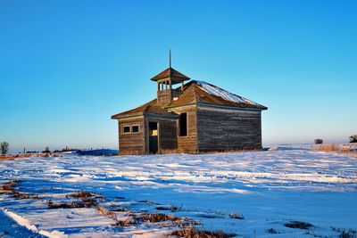 Building on snow covered field against clear blue sky