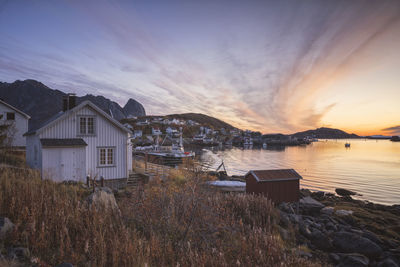 Buildings by lake against sky during sunset