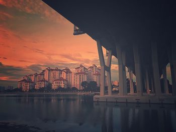 Bridge over river by buildings against sky during sunset