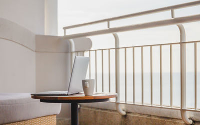 Open laptop with coffee cup on wood table on balcony with ocean view