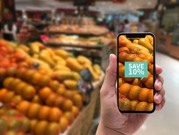 Cropped image of hand showing smart phone with discount at grocery store