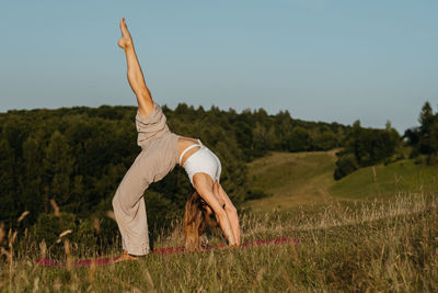 Young woman practicing yoga outdoors in the field with blue sky on the background