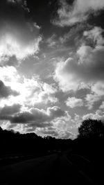 Road by silhouette trees against sky