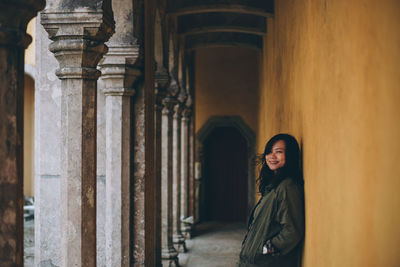 Side view portrait of smiling woman standing by columns