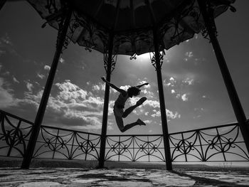 Low angle view of man jumping in gazebo against sky