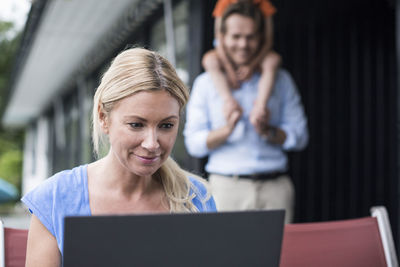 Woman using laptop at yard with family in background