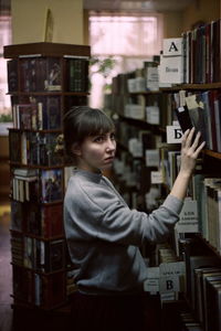 Side view of young woman searching book while standing in library