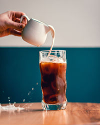 Midsection of person pouring drink in glass on table